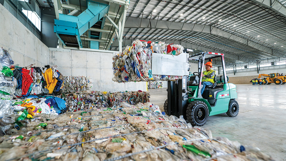 A construction vehicle placing bales of recycling materials in a warehouse storage space.