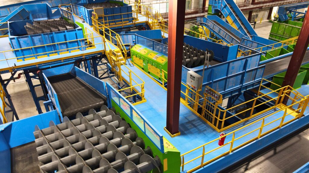 Overhead view of a colored industrial sorting plant with blue conveyors, screw rollers and yellow safety railings