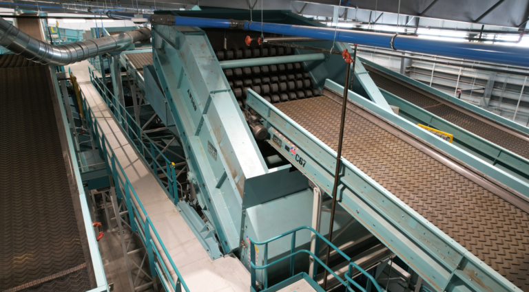 A modern industrial sorting and AWS Screen system with blue metal structures and various conveyor belts. The machinery appears designed for processing and sorting materials. Catwalks and railings provide access for workers to oversee operations safely.