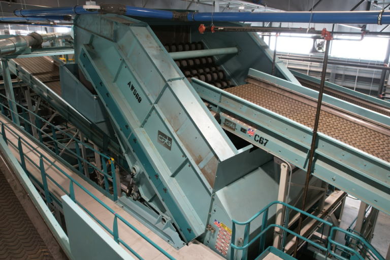 A large CP Screen machine with multiple conveyor belts and metal structures is seen in a factory or processing plant. The machinery appears to be used for material handling or sorting, with various paths and components leading in different directions.