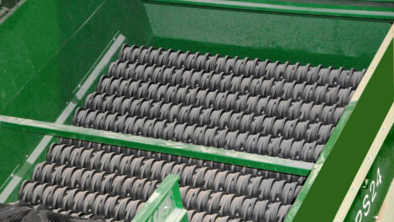 Close-up of a green CP Disc Screen machine featuring multiple black rolling elements arranged in rows, used for sorting, conveying, or processing agricultural products. The elements have a spiral pattern and are inside a green metallic frame.