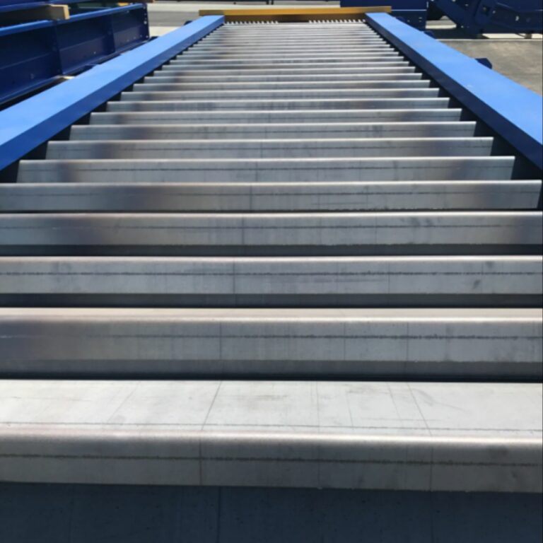 The image shows a straight set of outdoor steps with metallic surfaces, flanked by blue railings, against a blue sky. No people are visible.