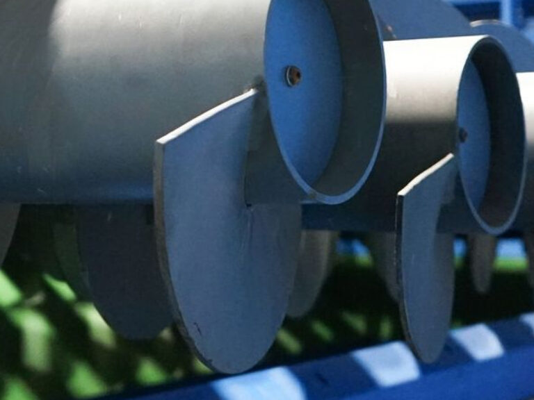 Close-up of a blue industrial auger with multiple screw blades in a row, set against a blurred background. The auger appears to be part of machinery, likely used for moving or processing materials.