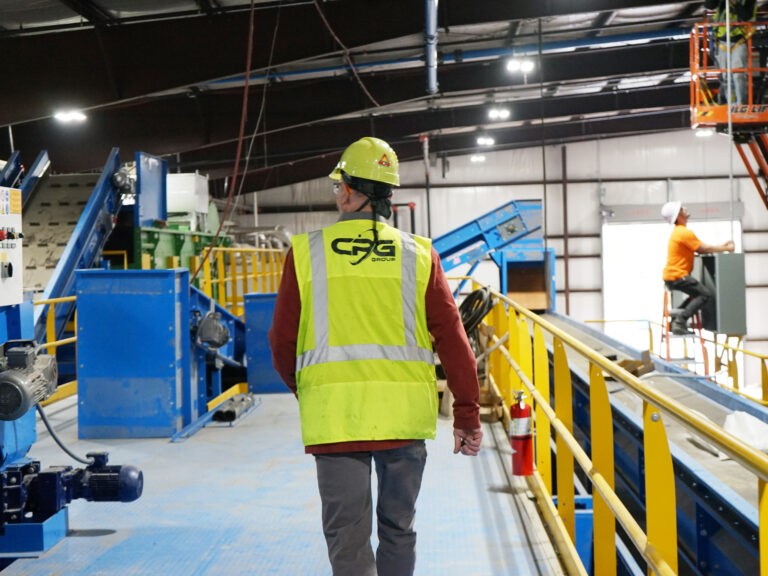 Image of a CPG employee wearing a safety vest and hard hat walking away in a MRF