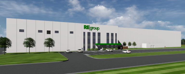 Large white industrial building with green REgroup logo, vertical glass entrance, green awning, parking lot and striped lawn.