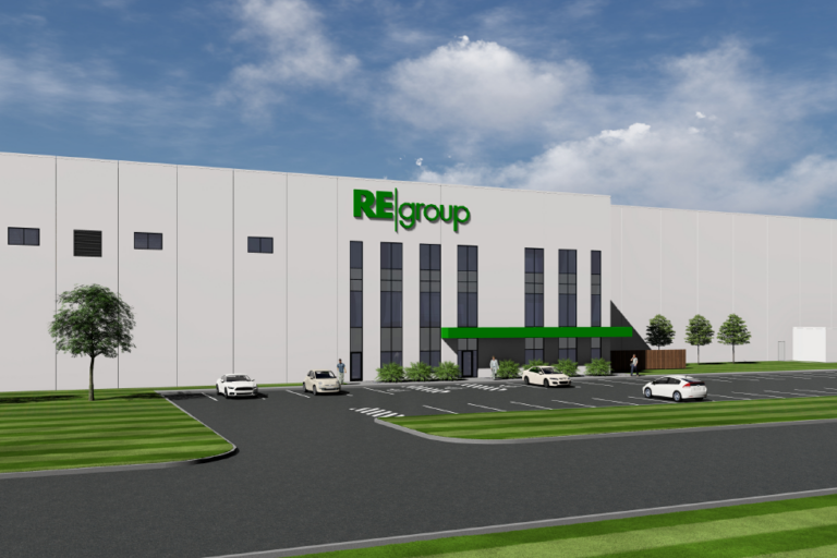 Large white industrial building with green REgroup logo, vertical glass entrance, green awning, parking lot and striped lawn.